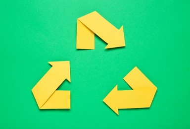 Photo of Recycling symbol made of yellow paper arrows on green background, top view