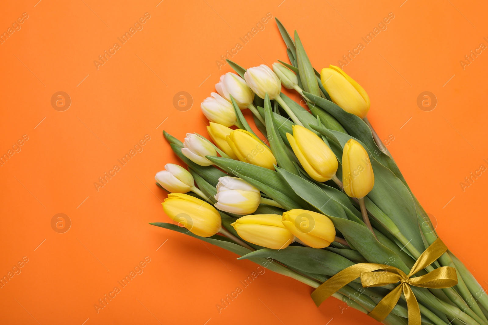 Photo of Bouquet of beautiful yellow tulips on orange background, top view. Space for text