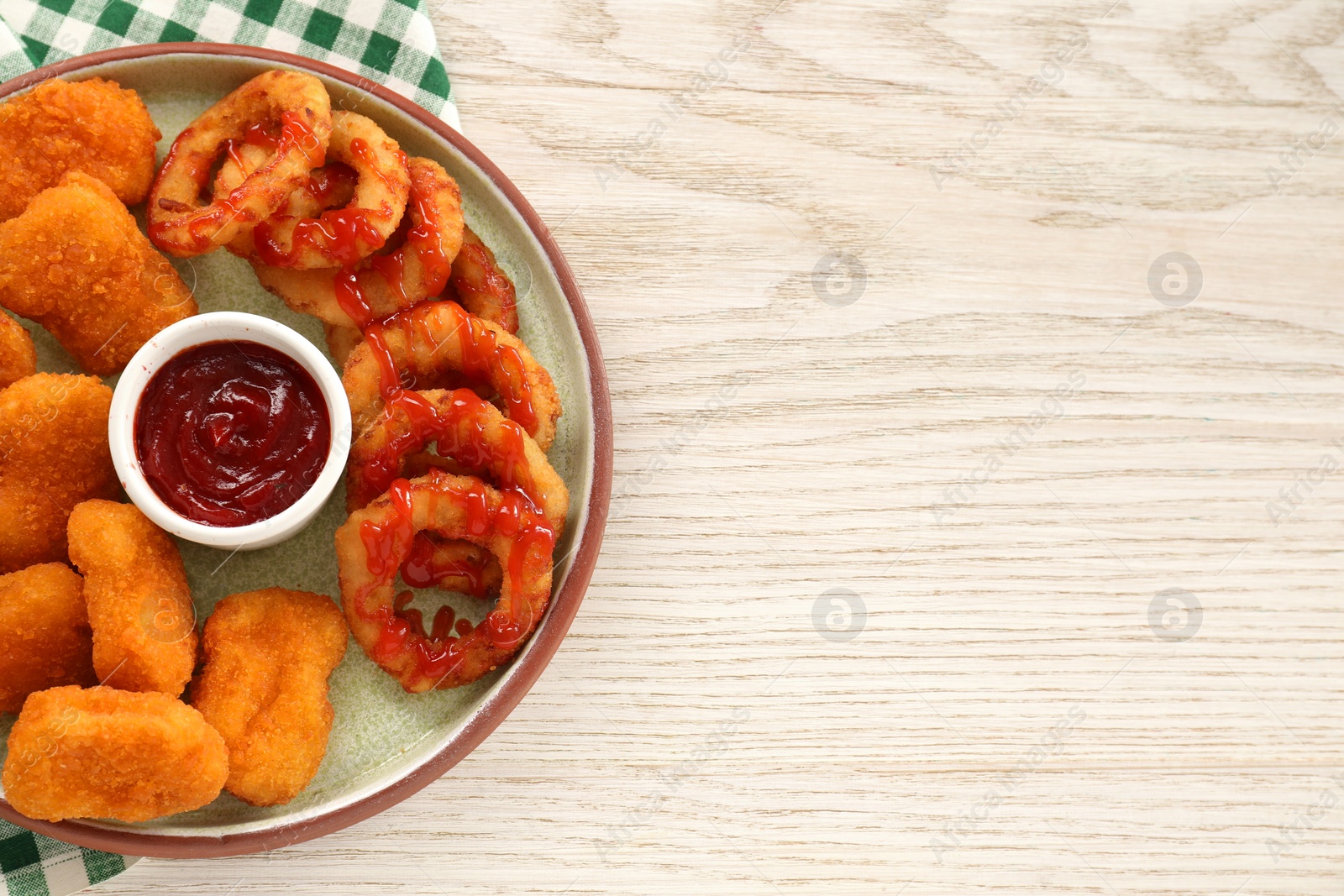 Photo of Tasty fried onion rings, chicken nuggets and ketchup on white wooden table, top view. Space for text
