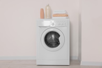 Photo of Modern washing machine, folded towels and bottles near white wall indoors