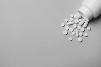 Bottle with different pills on grey background, flat lay. Space for text