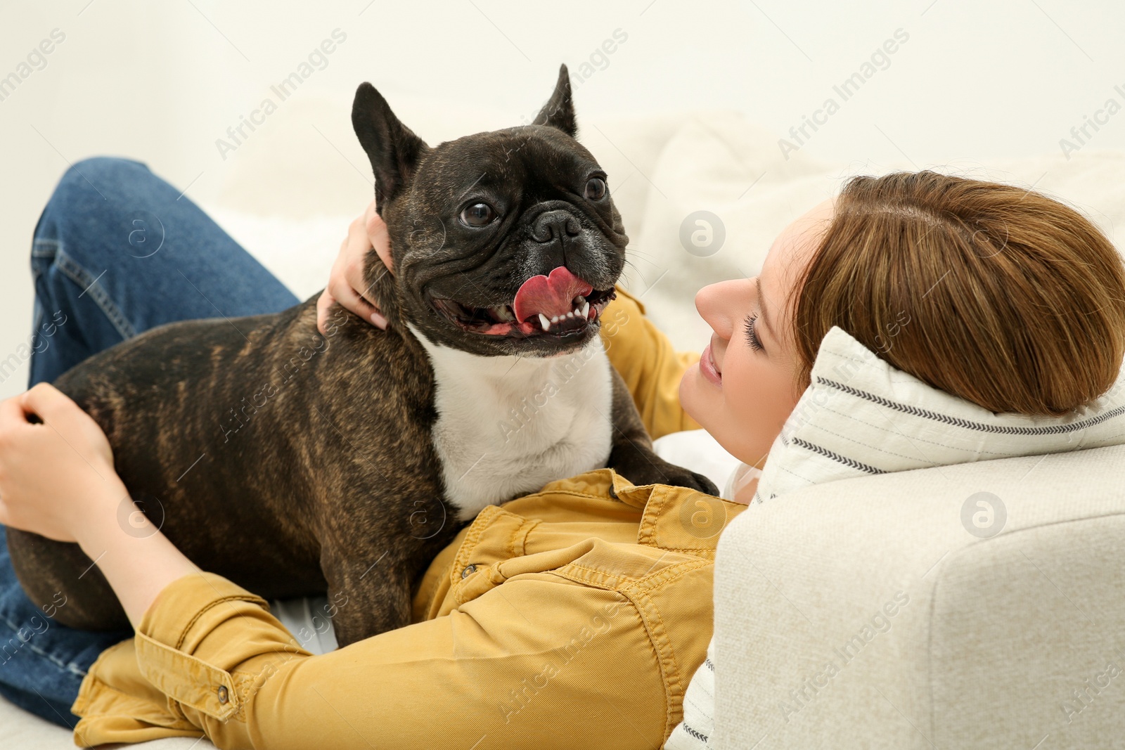 Photo of Woman with cute French Bulldog on soft sofa in room