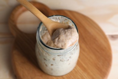 Photo of Taking sourdough starter with spoon at table, closeup