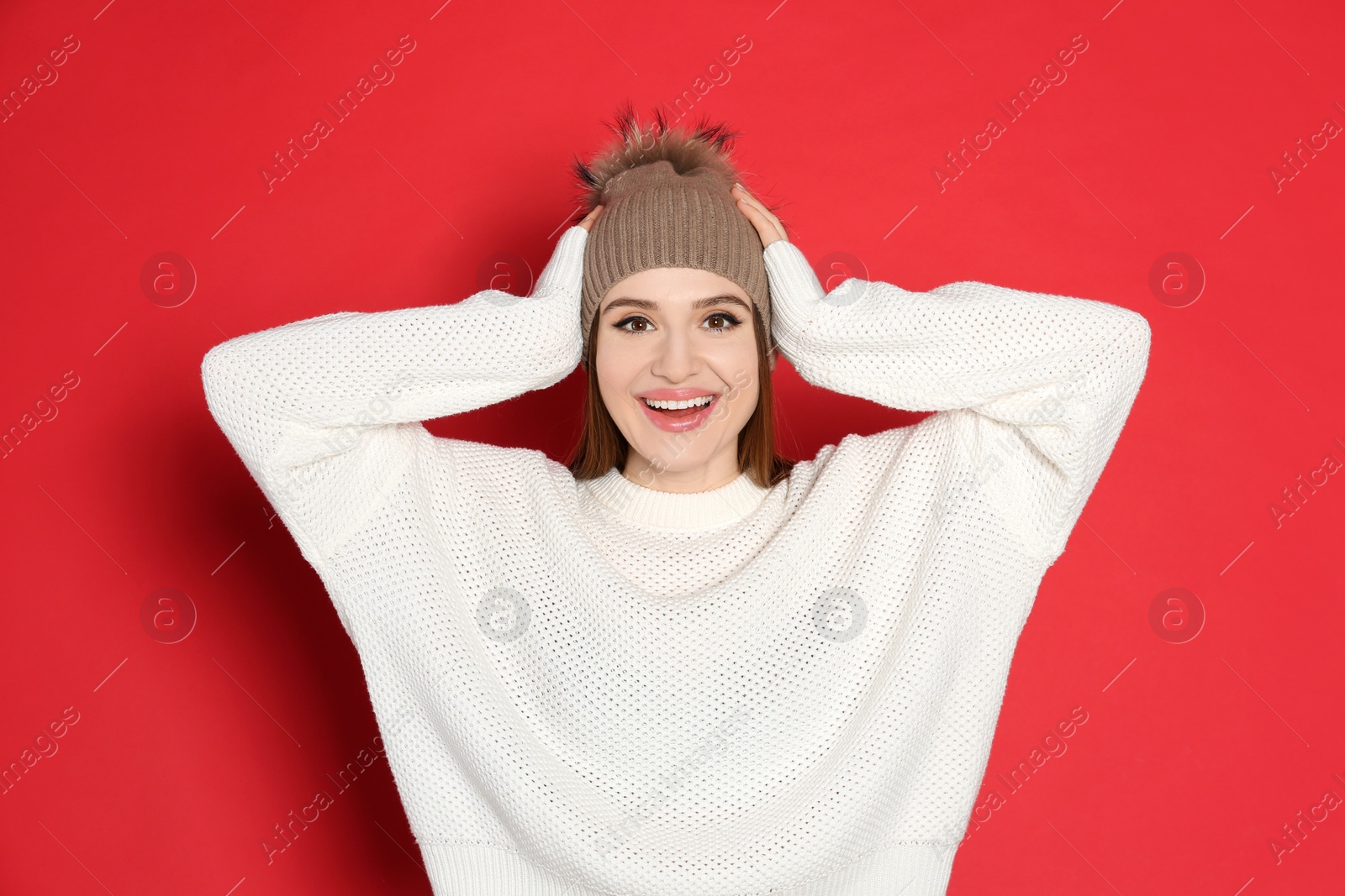 Photo of Young woman wearing warm sweater and hat on red background. Winter season