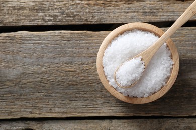 Organic salt in bowl and spoon on wooden table, top view. Space for text