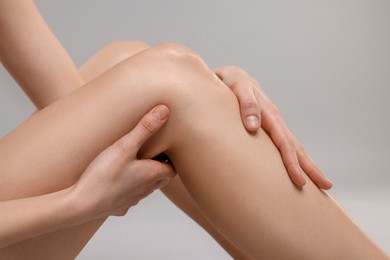 Photo of Woman suffering from leg pain on grey background, closeup