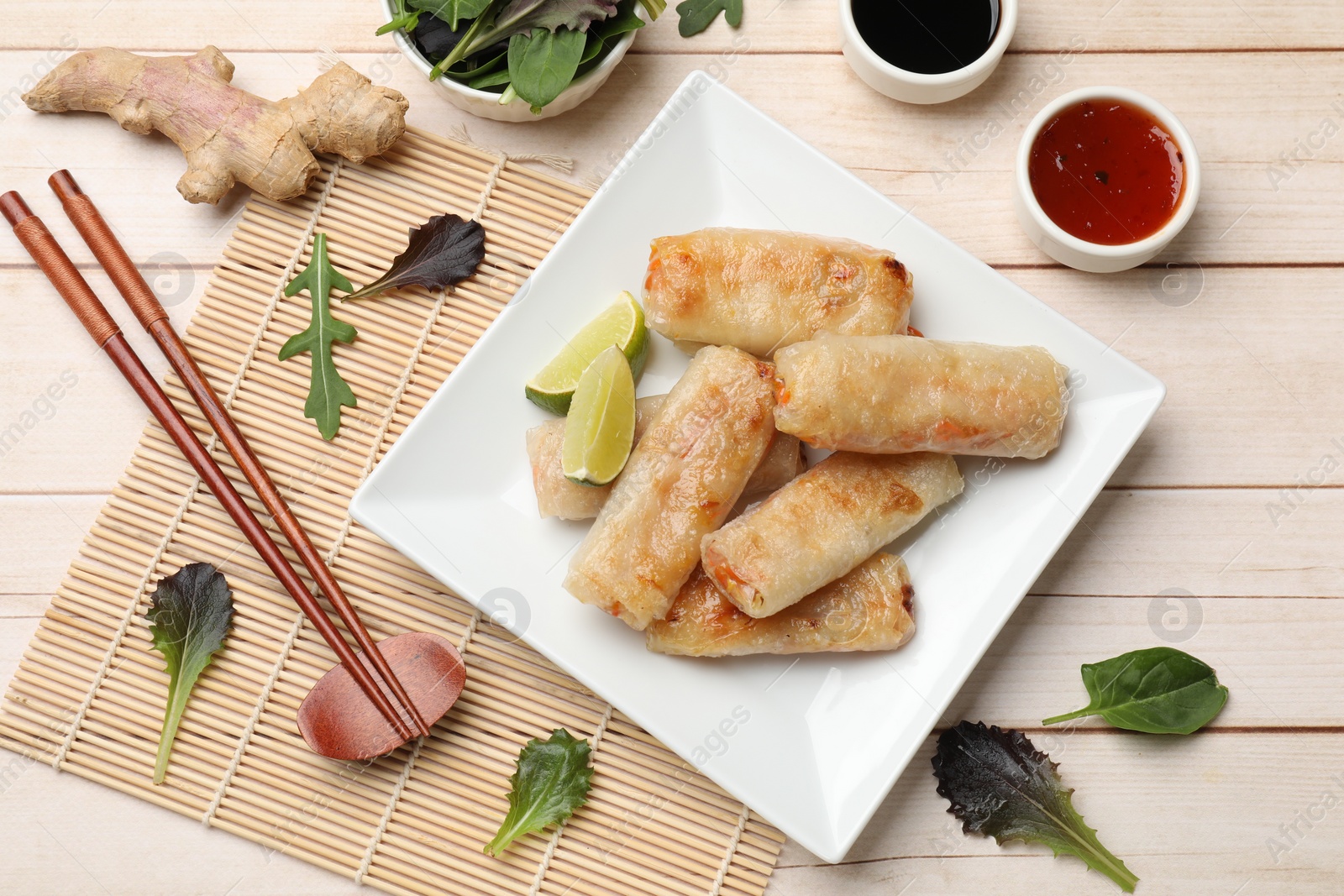 Photo of Tasty fried spring rolls, lime, sauces and other products on light wooden table, flat lay