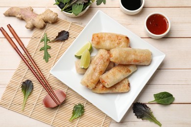 Photo of Tasty fried spring rolls, lime, sauces and other products on light wooden table, flat lay