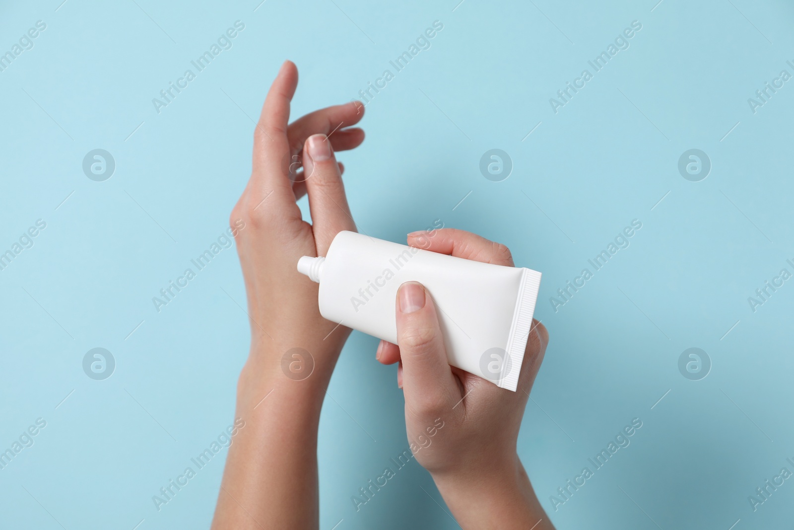 Photo of Woman applying cosmetic cream from tube onto her hand on light blue background, top view