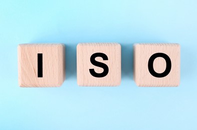 Photo of International Organization for Standardization. Wooden cubes with abbreviation ISO on light blue background, top view