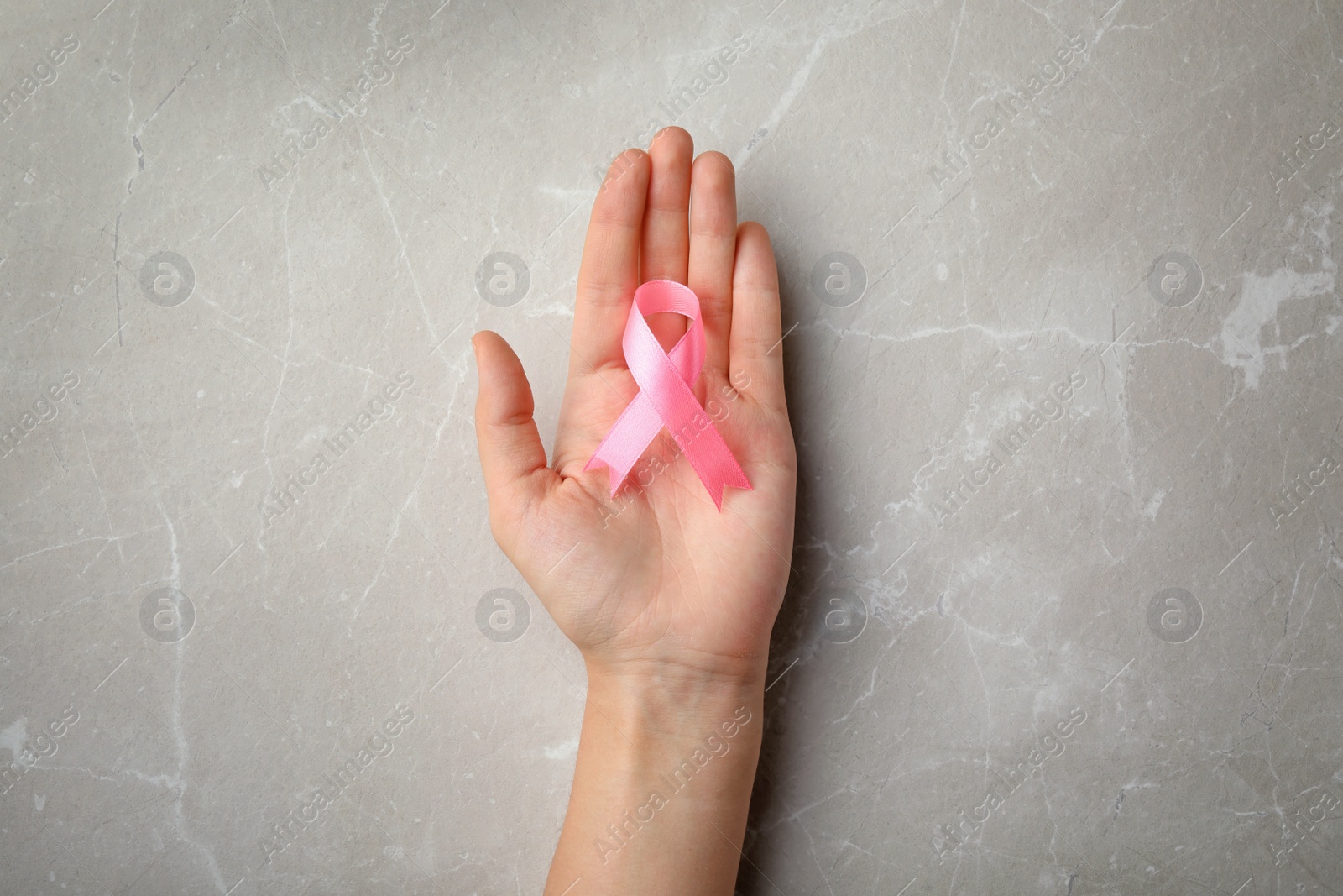 Photo of Woman holding pink ribbon on grey background, top view. Breast cancer awareness concept