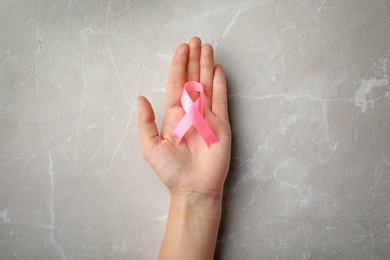 Woman holding pink ribbon on grey background, top view. Breast cancer awareness concept