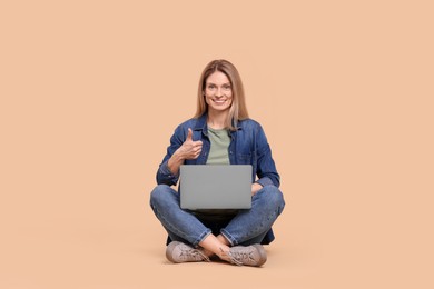 Photo of Happy woman with laptop showing thumb up on beige background
