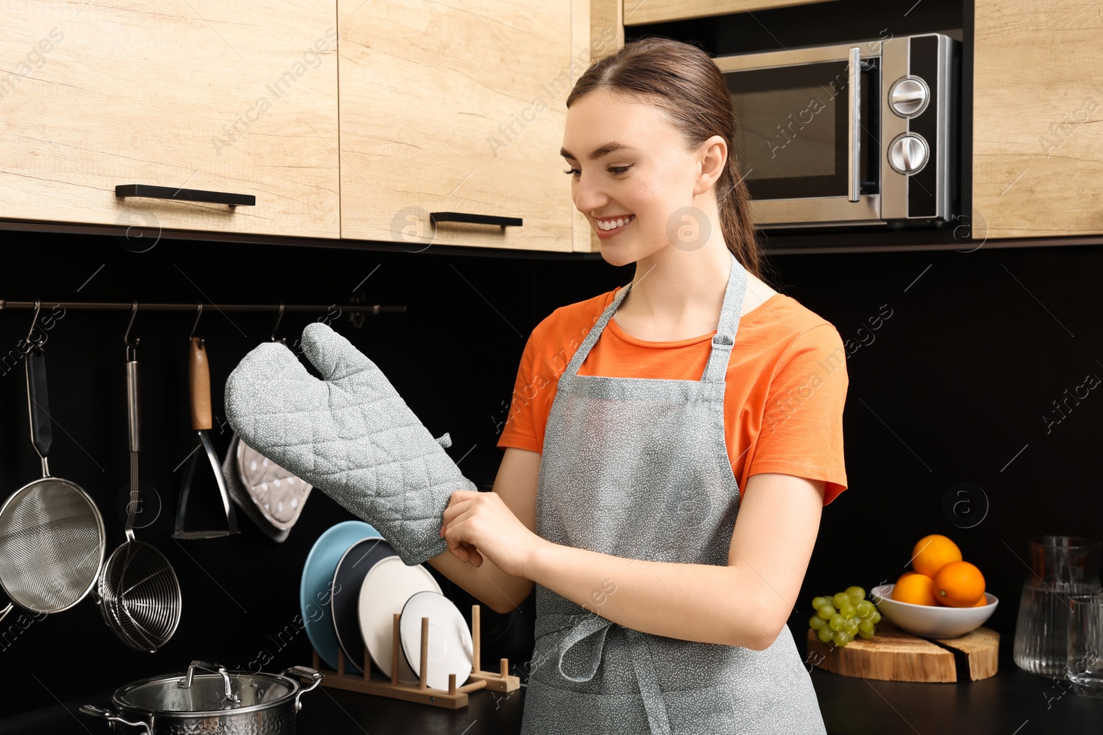 Photo of Beautiful young woman in clean apron and oven glove at kitchen