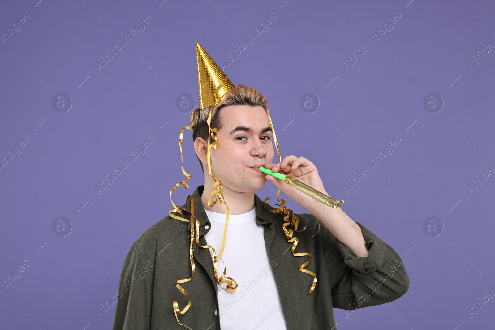 Photo of Young man with party hat and blower on purple background