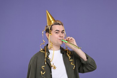 Young man with party hat and blower on purple background