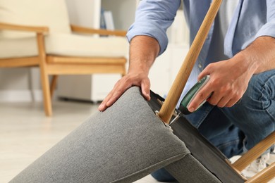 Photo of Man with electric screwdriver assembling armchair at home, closeup