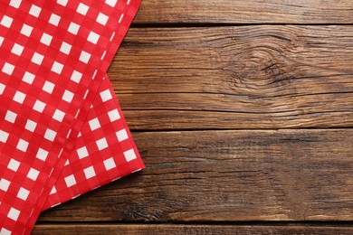 Photo of Red checkered tablecloth on wooden table, top view. Space for text