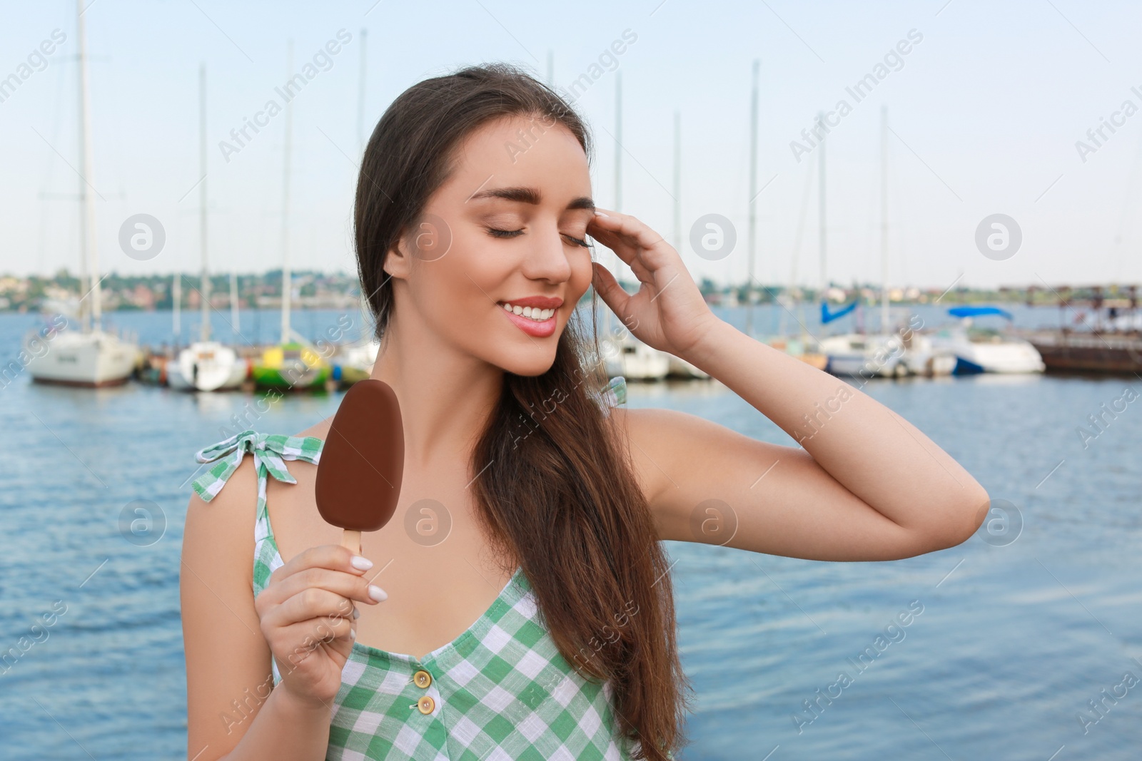 Photo of Beautiful young woman holding ice cream glazed in chocolate near river