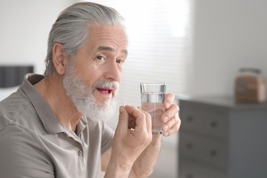 Photo of Senior man with glass of water taking pill indoors