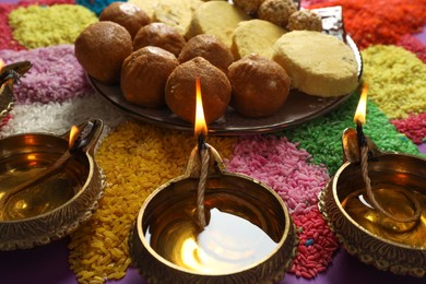 Photo of Diwali celebration. Tasty Indian sweets, diya lamps and colorful rangoli on table, closeup