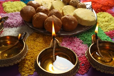 Diwali celebration. Tasty Indian sweets, diya lamps and colorful rangoli on table, closeup