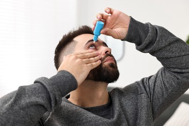 Young man applying medical eye drops indoors