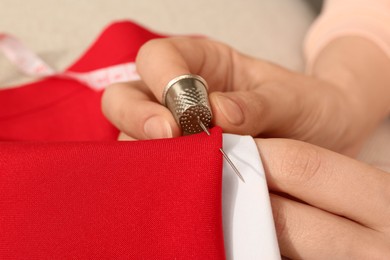 Photo of Woman sewing on red fabric with thimble and needle, closeup