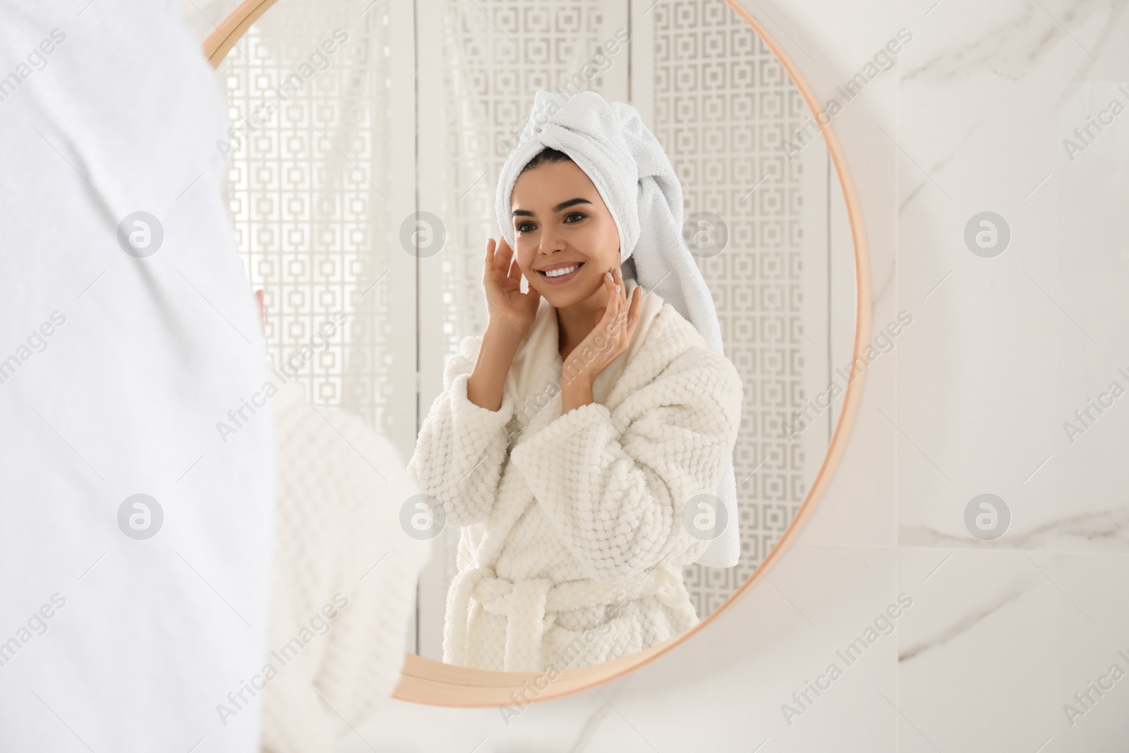 Photo of Young woman with hair wrapped in towel near mirror indoors