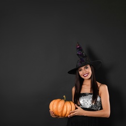 Photo of Beautiful woman wearing witch costume with pumpkin for Halloween party on black background, space for text