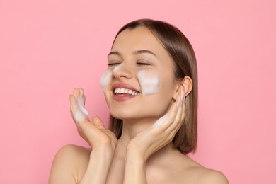 Photo of Young woman washing face with cleansing foam on pink background. Skin care cosmetic