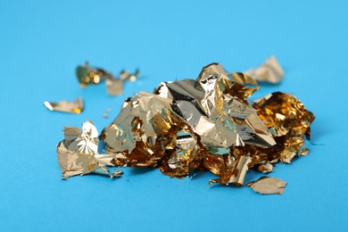 Photo of Pieces of edible gold leaf on light blue background, closeup