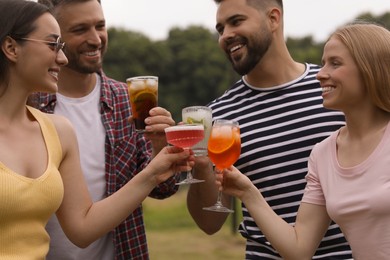 Photo of Happy friends clinking glasses with cocktails outdoors