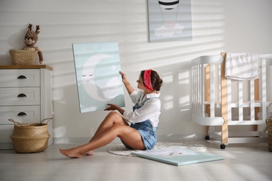 Photo of Decorator with picture on floor in baby room. Interior design