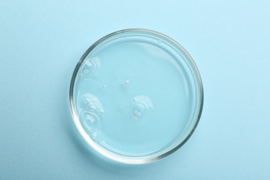 Photo of Petri dish with liquid sample on light blue background, top view