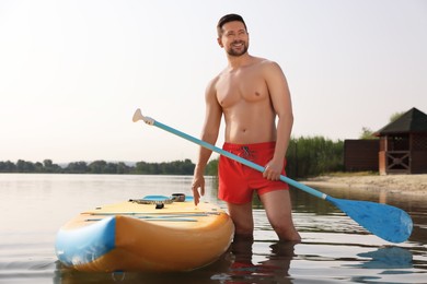 Photo of Man with paddle standing near SUP board in water