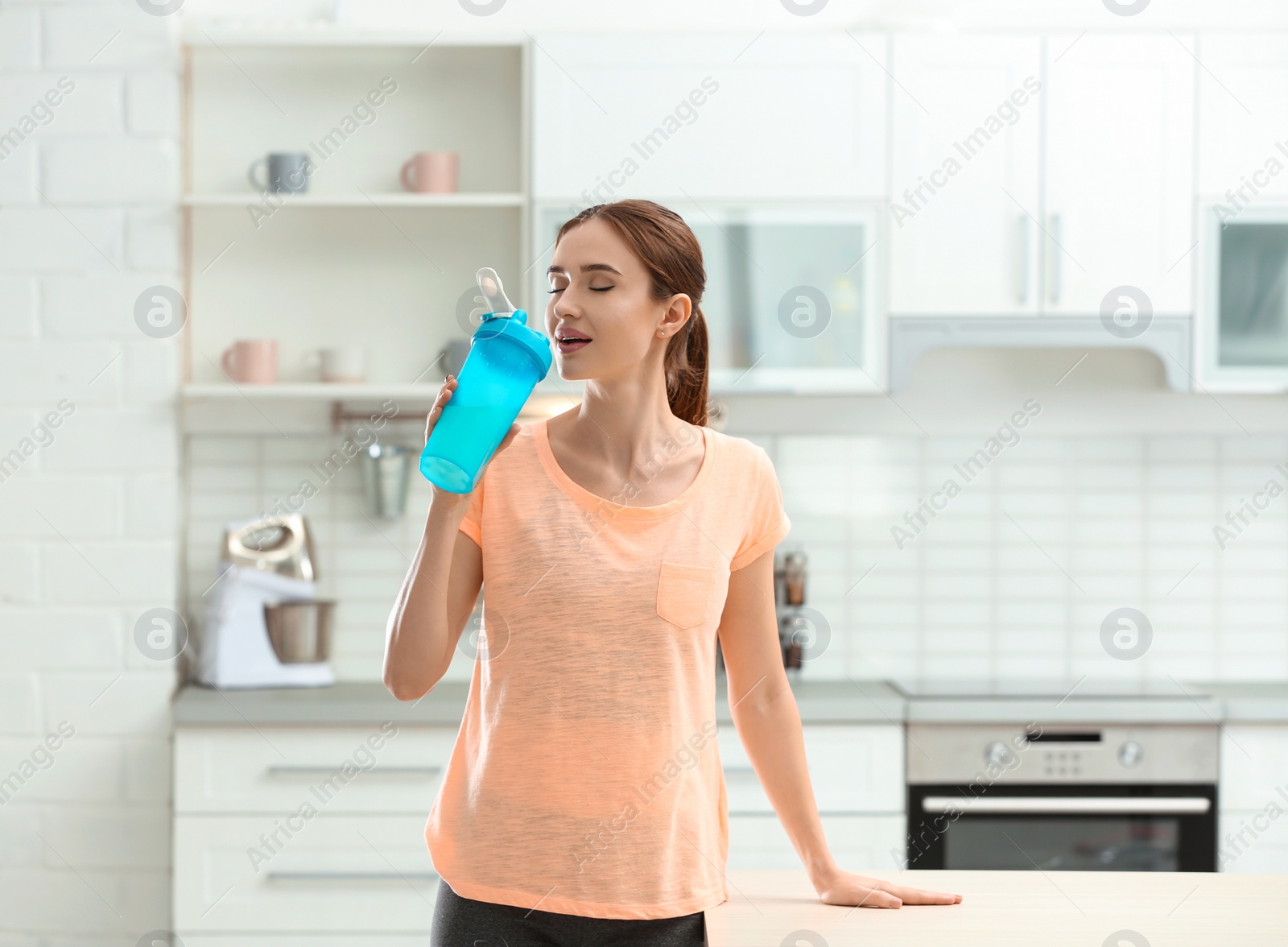 Photo of Athletic young woman drinking protein shake in kitchen