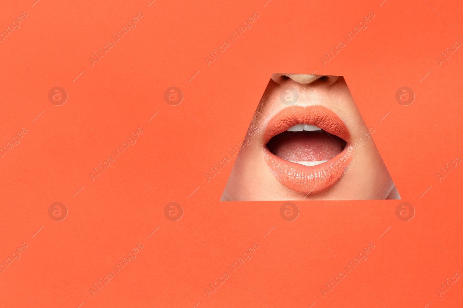 Photo of Lips of young woman with beautiful lipstick visible through hole in color paper. Space for text