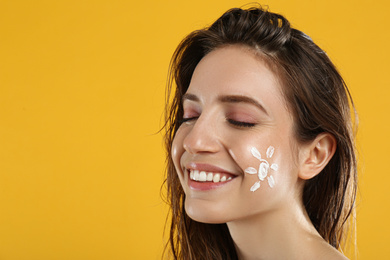 Photo of Young woman with sun protection cream on face against yellow background. Space for text