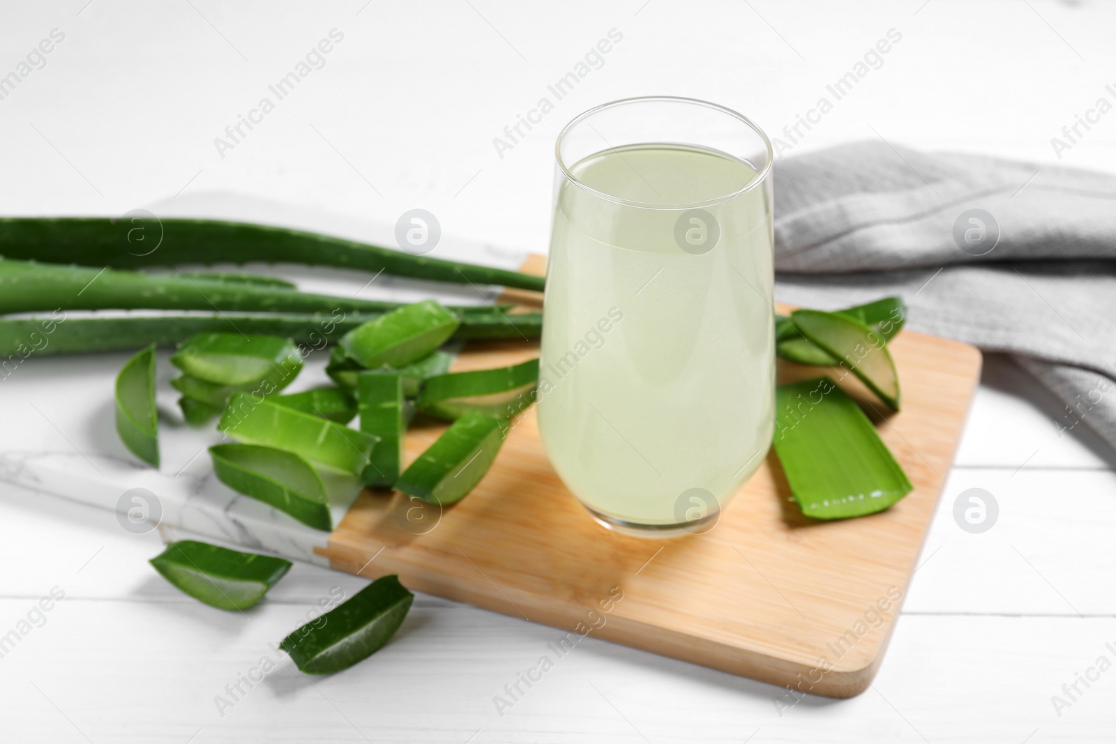 Photo of Fresh aloe juice in glass and leaves on white wooden table, closeup