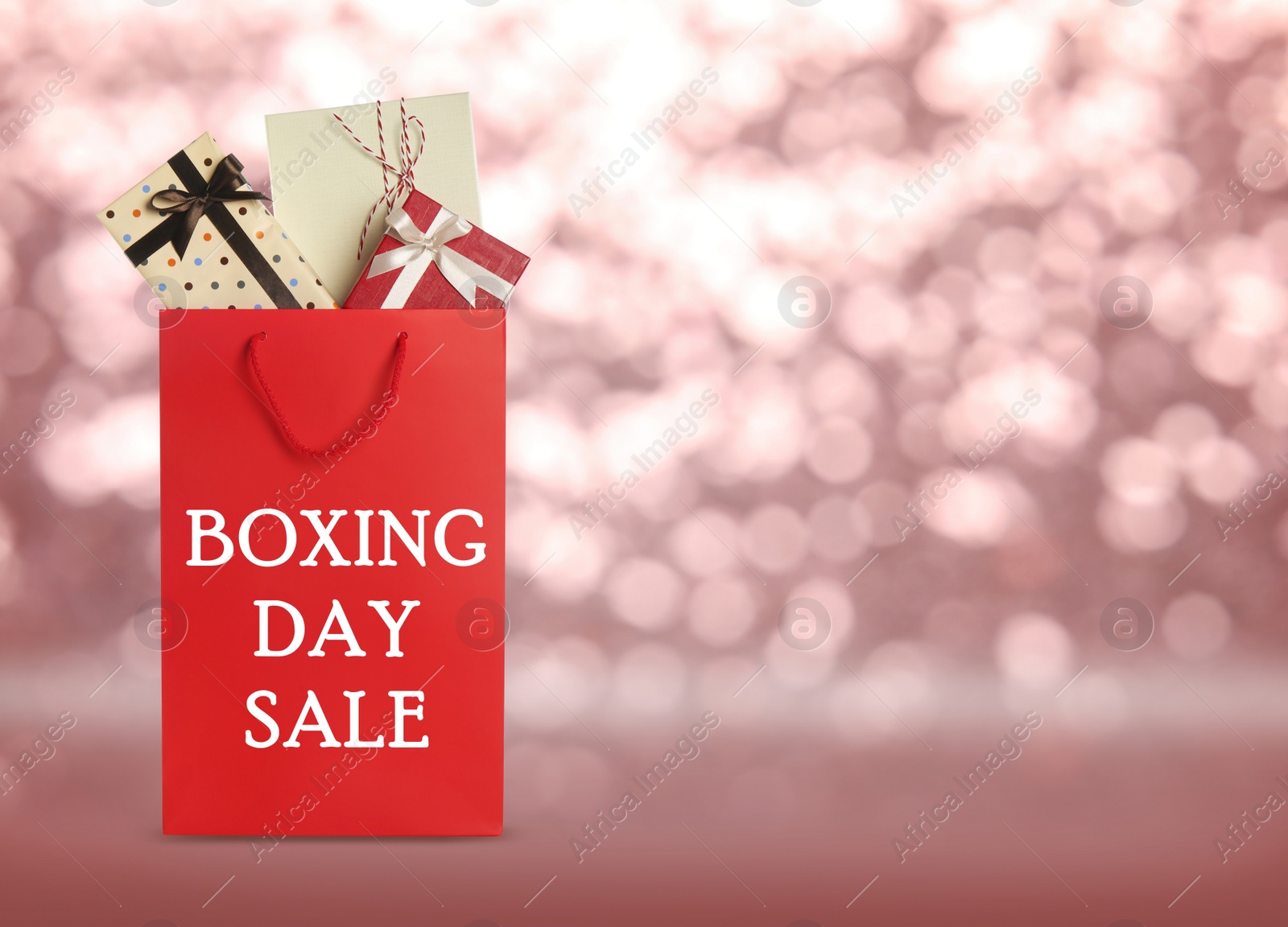 Image of Red shopping bag with text Boxing Day Sale full of gifts on blurred pink background, closeup. Space for text