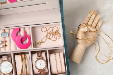 Photo of Jewelry box with many different accessories and mannequin hand on light grey table, flat lay