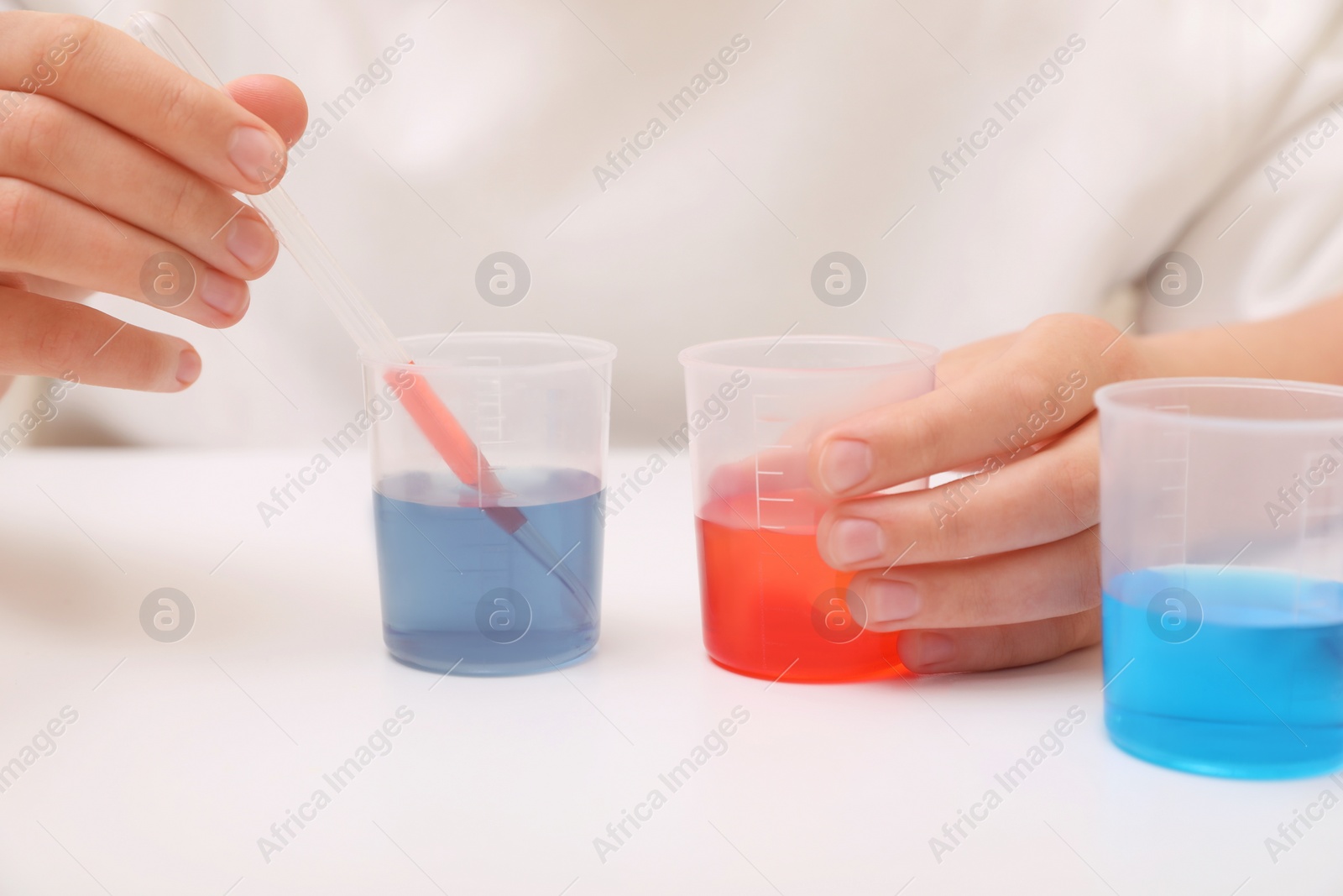 Photo of Girl mixing colorful liquids at white table indoors, closeup. Chemical experiment set for kids