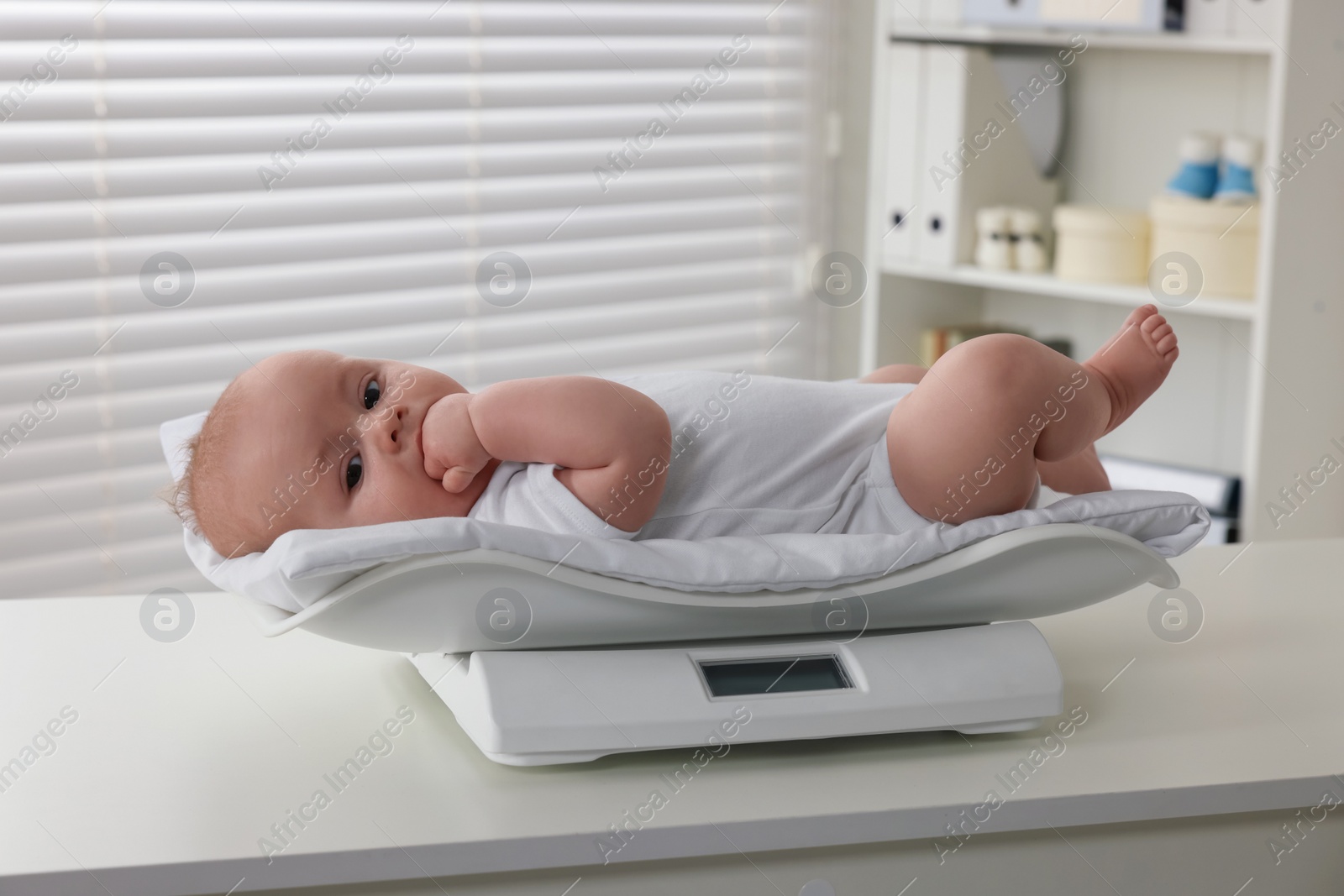 Photo of Cute little baby lying on scales in clinic