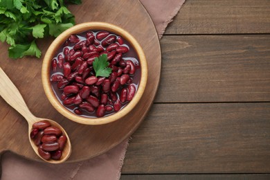Photo of Bowl of canned red kidney beans, parsley and spoon on wooden table, flat lay. Space for text