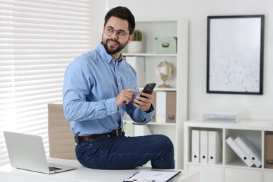 Photo of Happy young man using smartphone in office