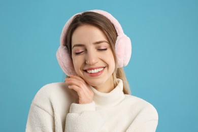 Happy woman wearing warm earmuffs on light blue background