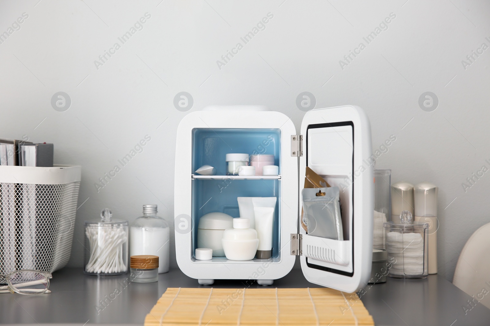 Photo of Mini fridge with cosmetic products on grey vanity table indoors