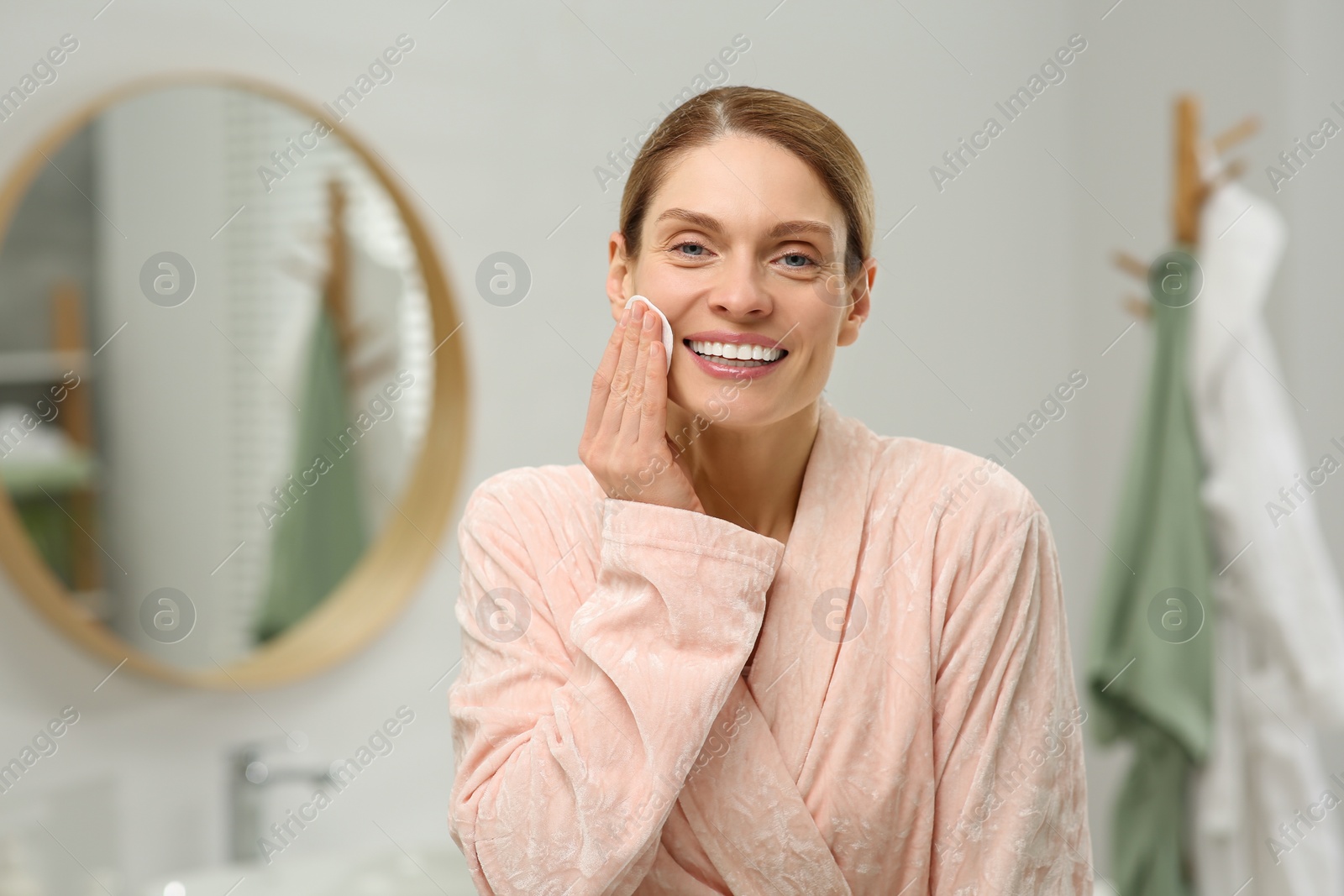 Photo of Beautiful woman removing makeup with cotton pad indoors, space for text