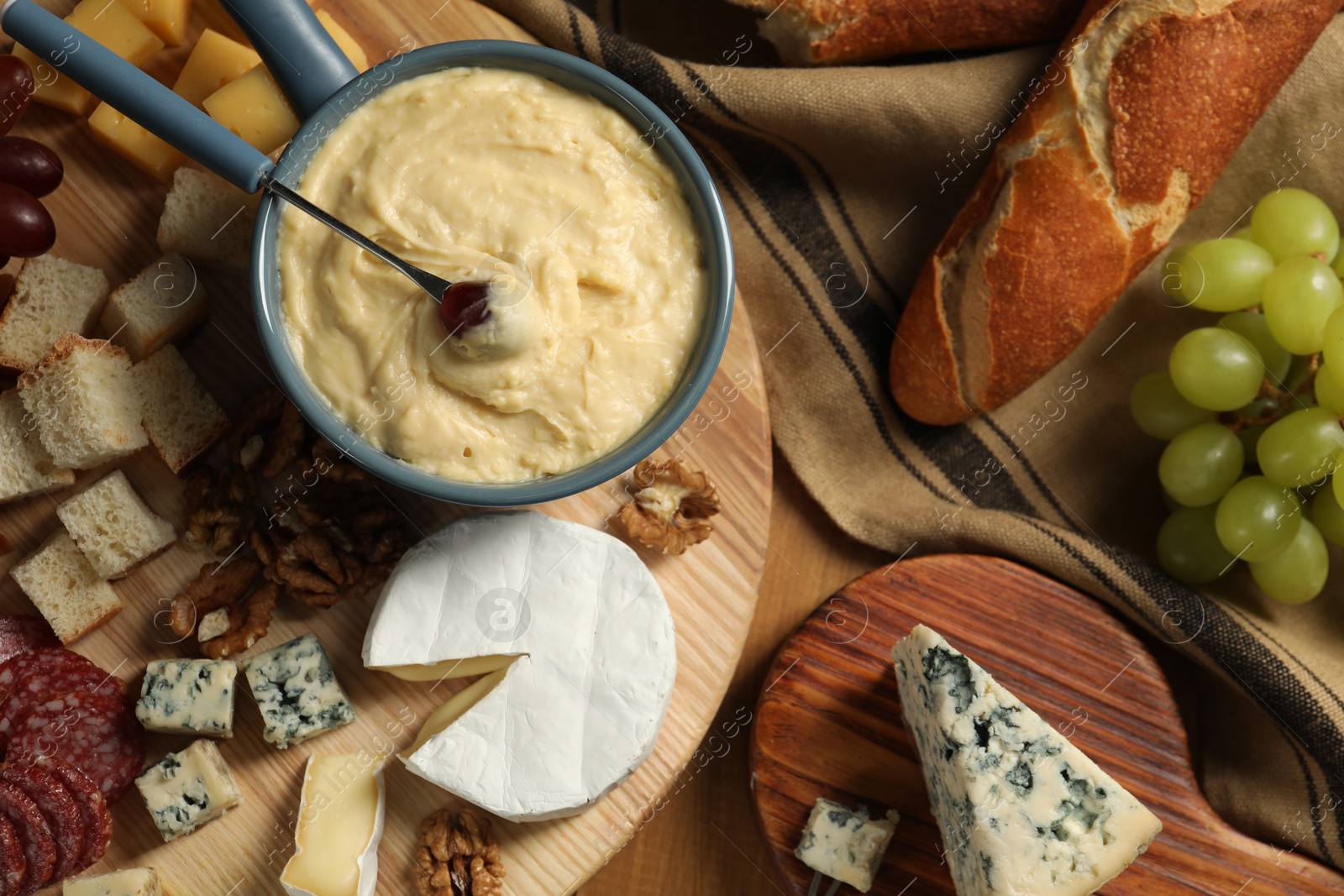 Photo of Fondue pot with tasty melted cheese, fork and different snacks on wooden table, top view